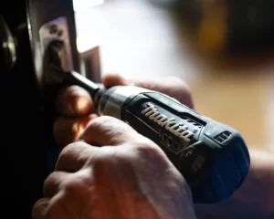Man using a power drill to install a door latch in a wooden door frame