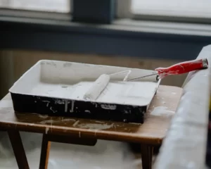 A paint roller dipped in white paint sits in a pan on a tabletop ready for use.