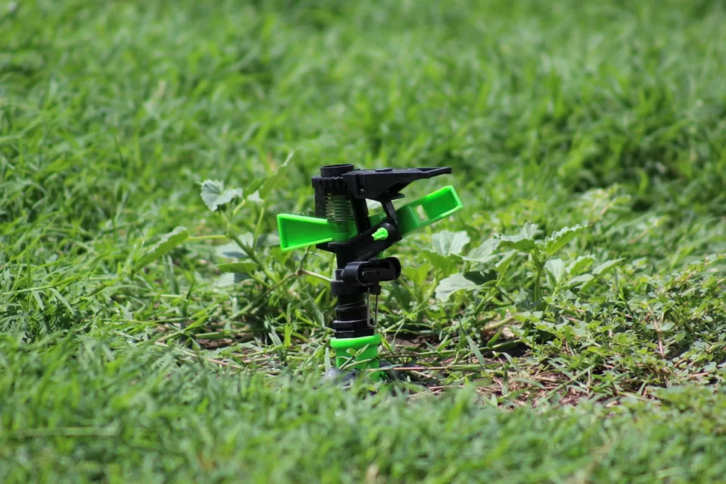 An inground lawn sprinkler head, with green grass and dirt visible in the background.