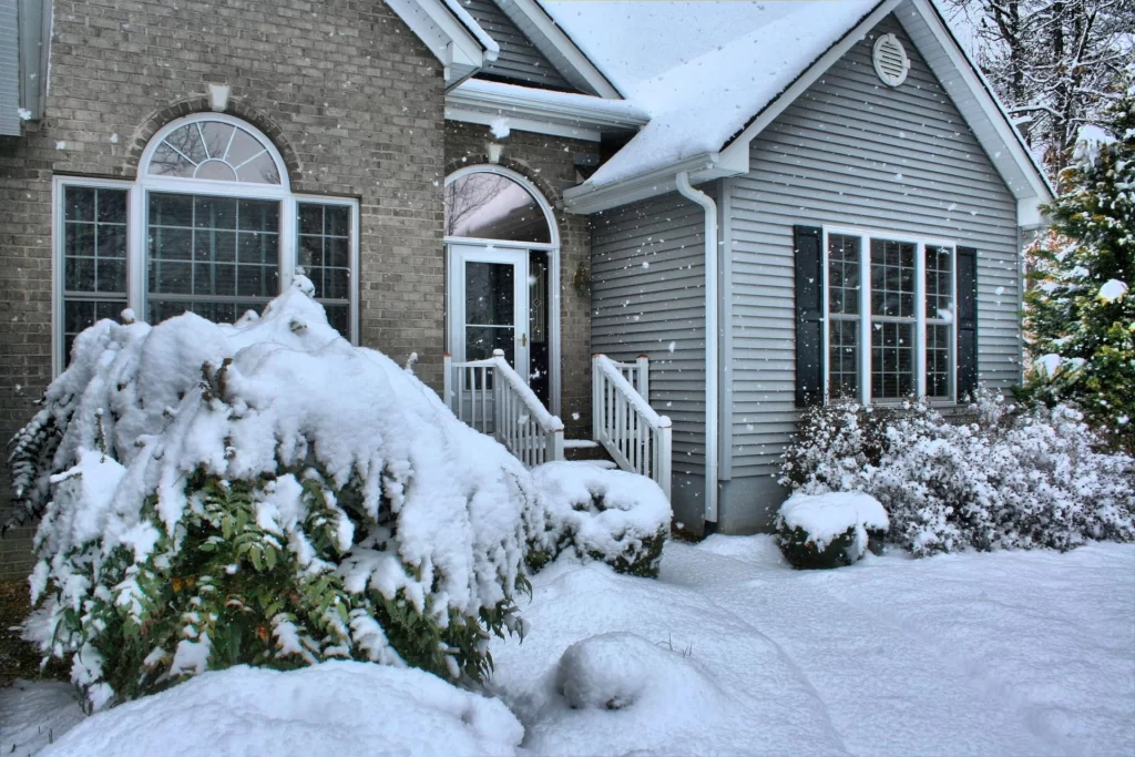 A house covered in a thick blanket of snow, with icicles hanging from the roof and snow piled up around the base.