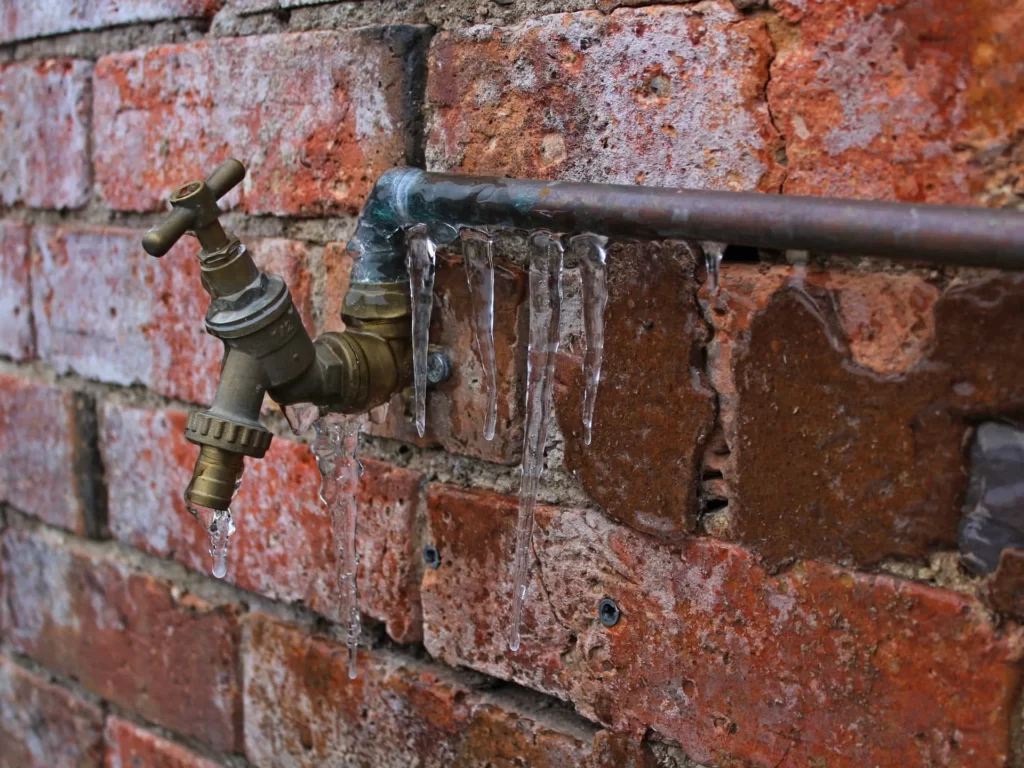 An outdoor water spigot that appears to be broken or not functioning, with water dripping from the disconnected hose.