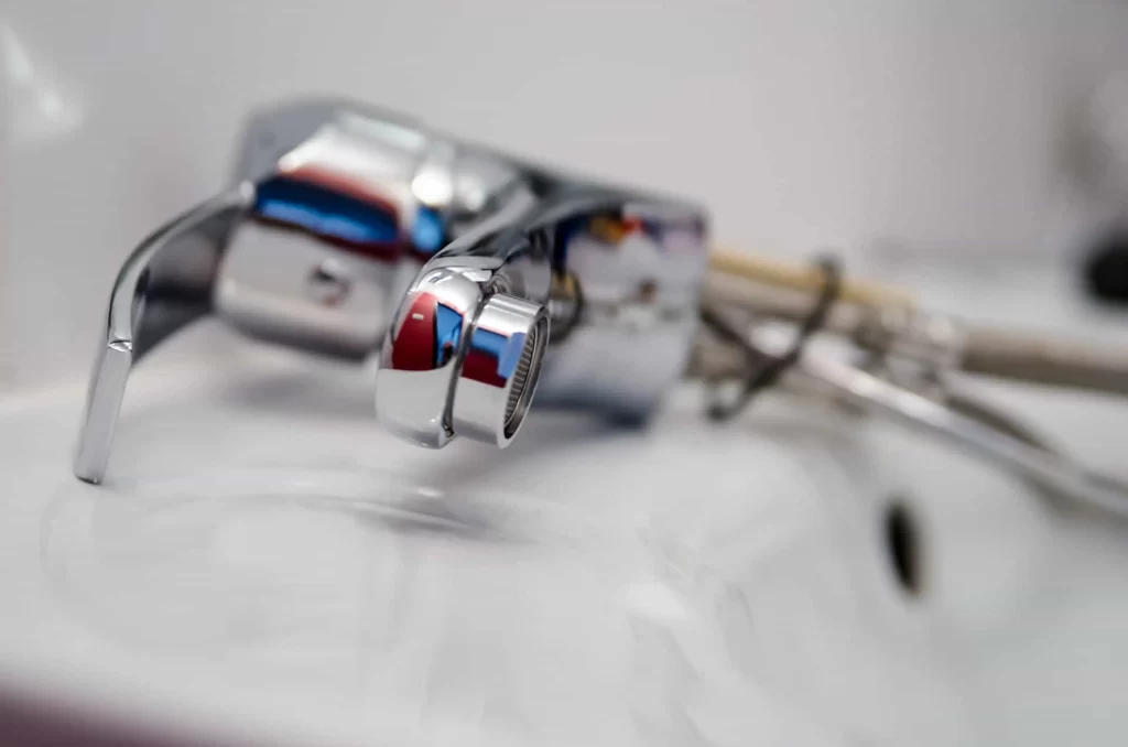 A faucet laying on a bathroom sink, with mounting hardware and pipes visible, indicating it is ready to be installed.